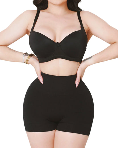 Person wearing a black bra and high-waisted shorts on a plain background